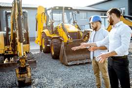 Cette photo montre deux professionnels du bâtiment discutant devant un engin de chantier. (Image : image Adobe Stock)