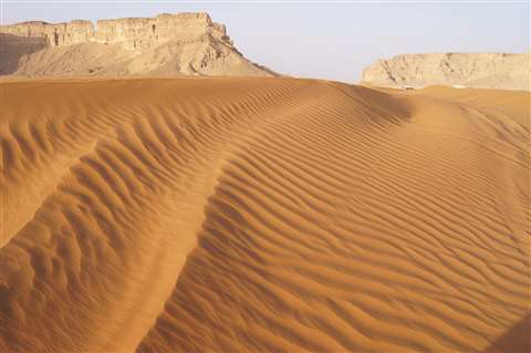 Sand dunes with rock formations in background taken at the Red Sands, Riyadh, Kingdom of Saudi Arabia.